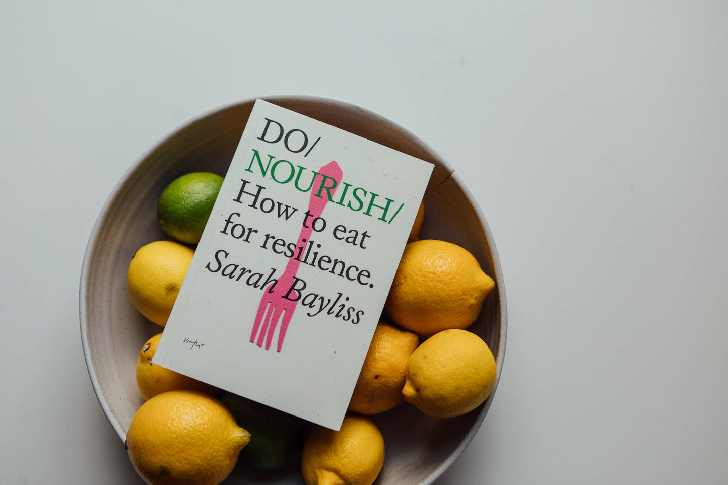 Book titled 'Do Nourish' by Sarah Bayliss surrounded by lemons and limes on a light background