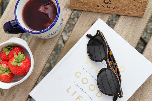 Sunglasses on a book with a cup of tea and strawberries on a wooden table