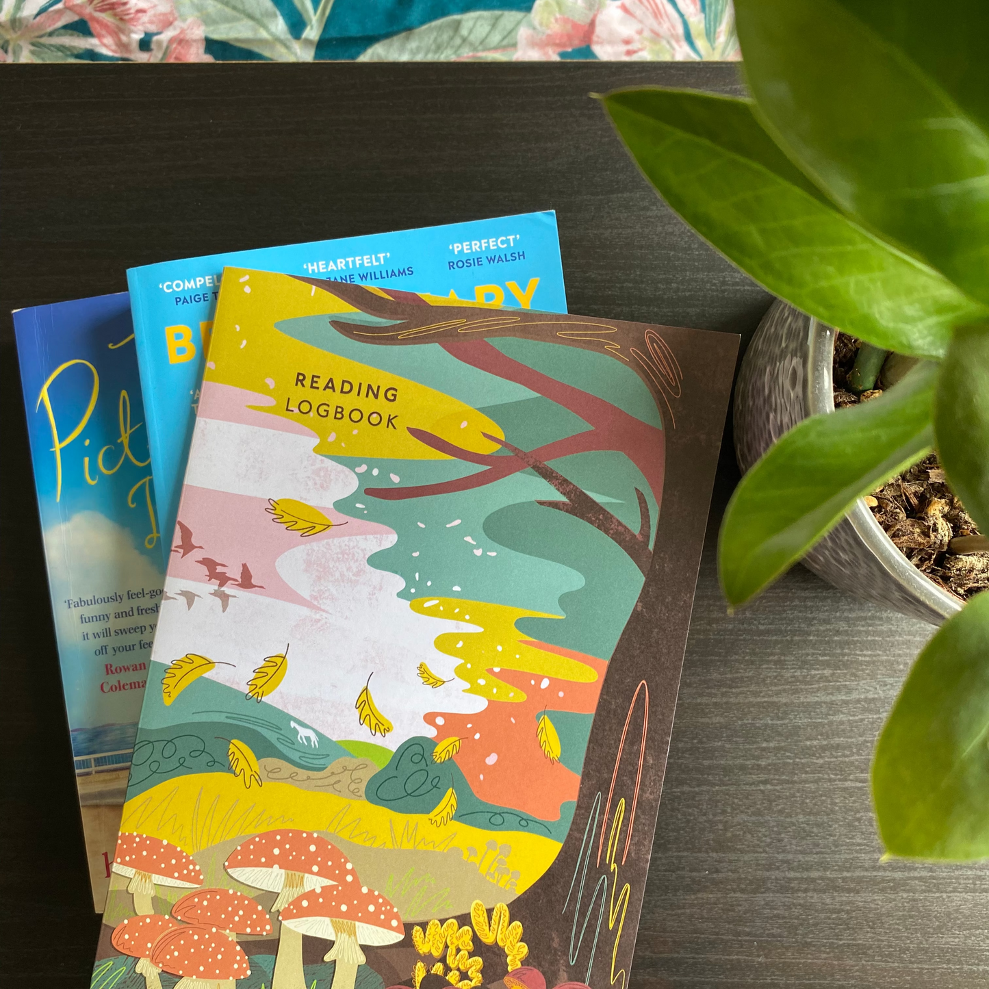 Colorful reading logbook with nature-themed design on a wooden surface with a plant in the background.