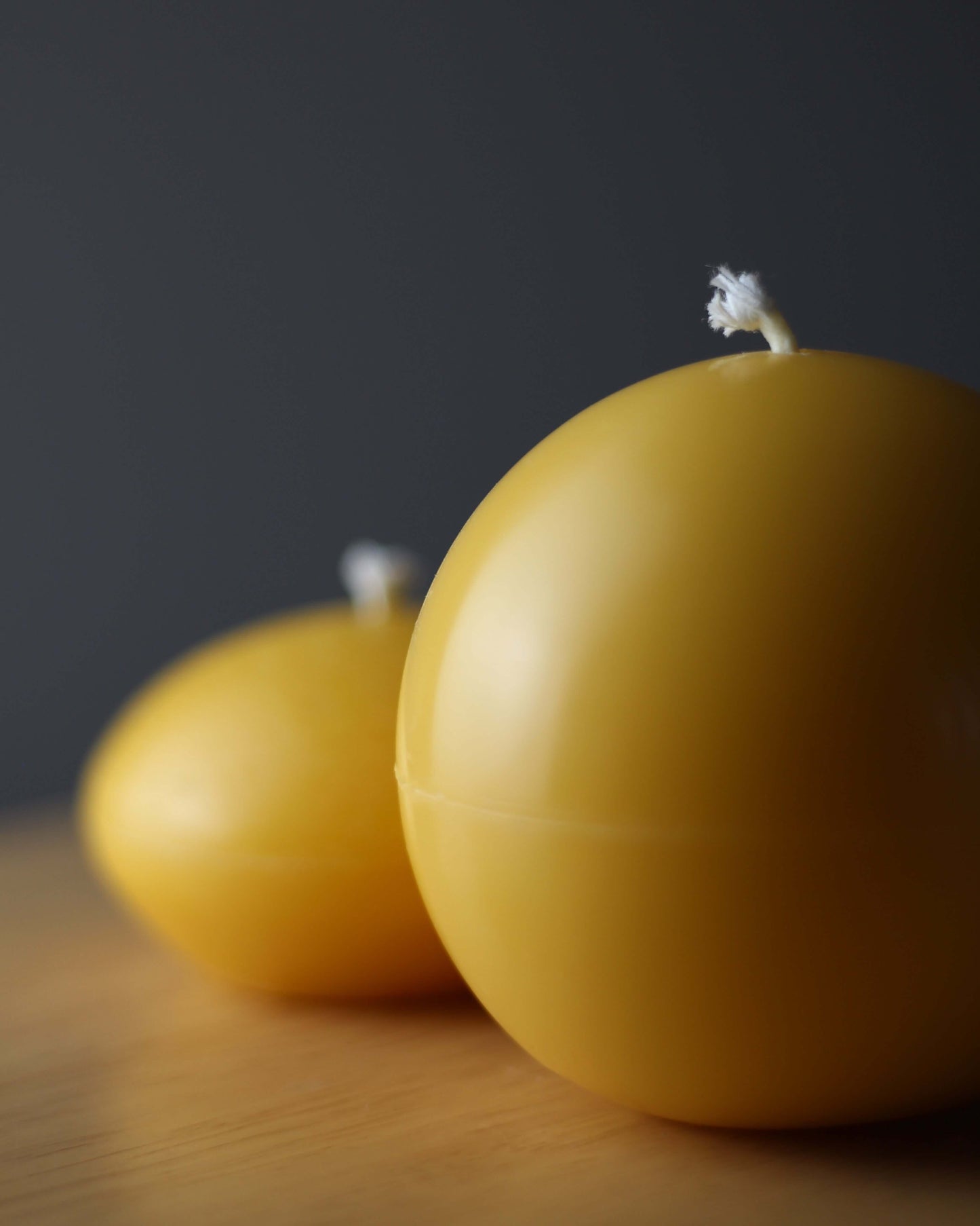 Ball & Ellipse set of 2 yellow beeswax ball shaped candles on a wooden surface.