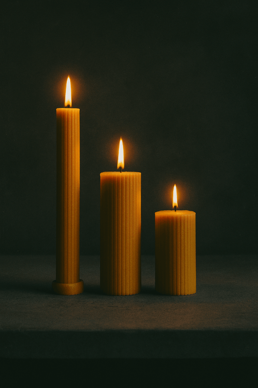Cylinders: set of 3 beeswax pillar candles in different heights, glowing with warm candlelight on a dark background.