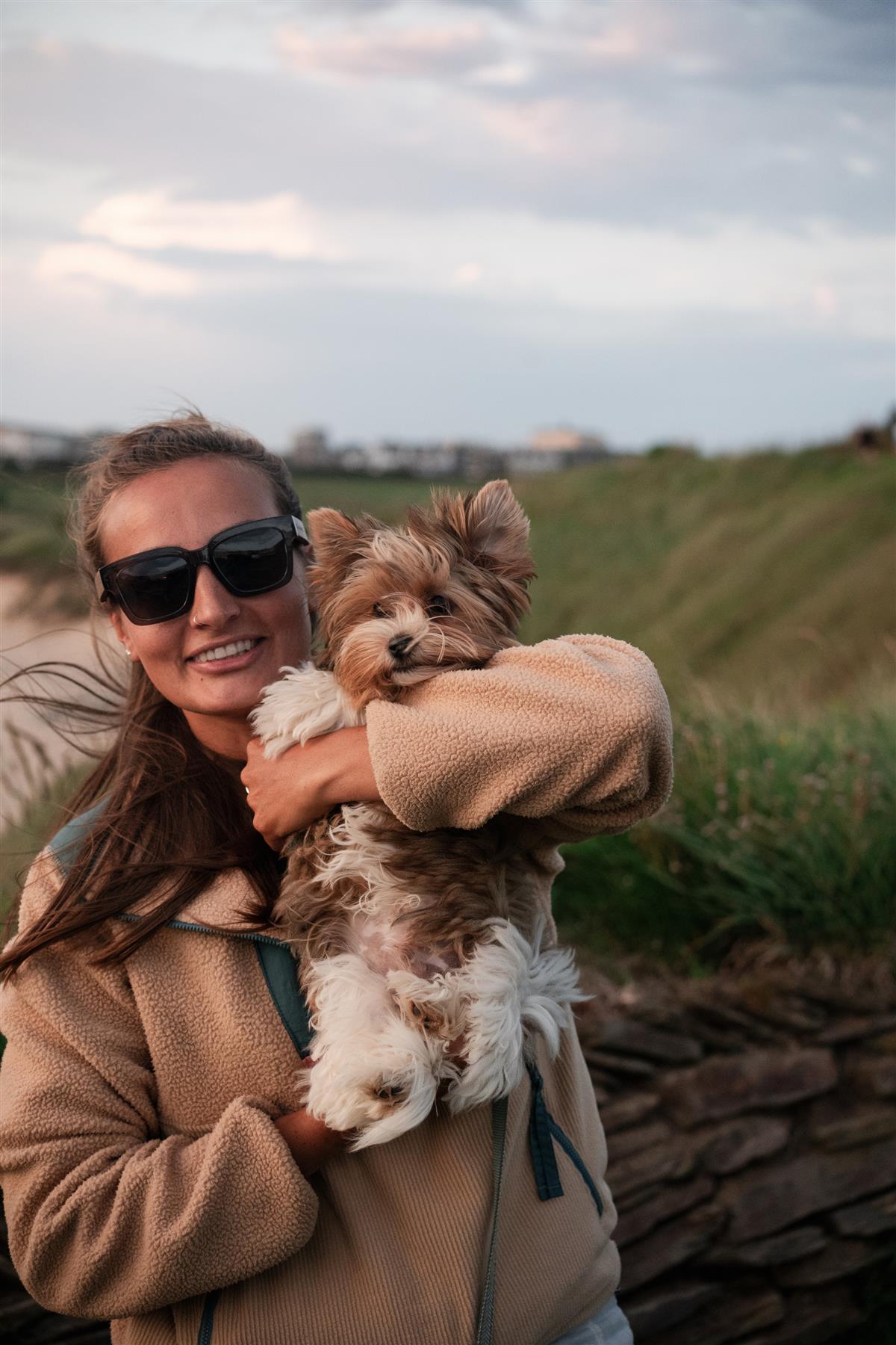 Woman holding a small dog outdoors with a scenic background