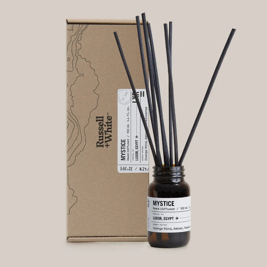 Mystice hand diffuser with black reeds and a brown box on a beige background