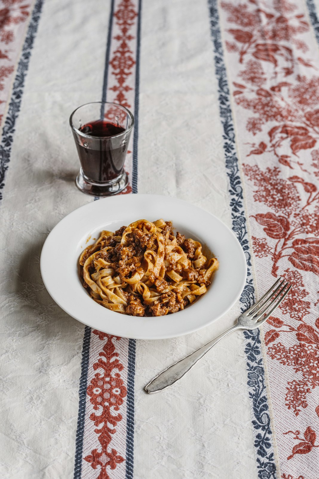 Pasta dish with a glass of red wine on a patterned tablecloth