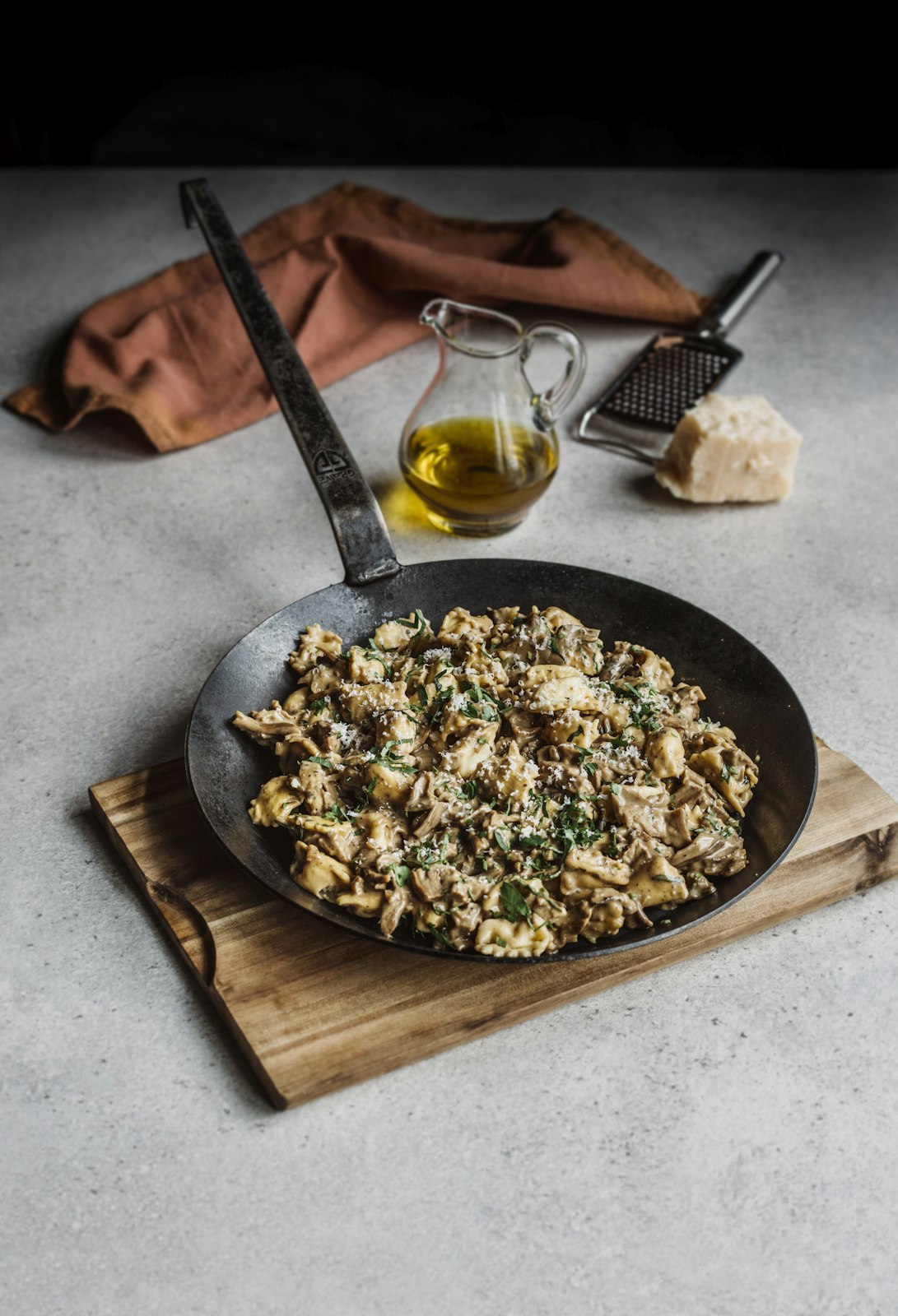 Fried eggs in a pan on a wooden board with olive oil and cheese in the background.