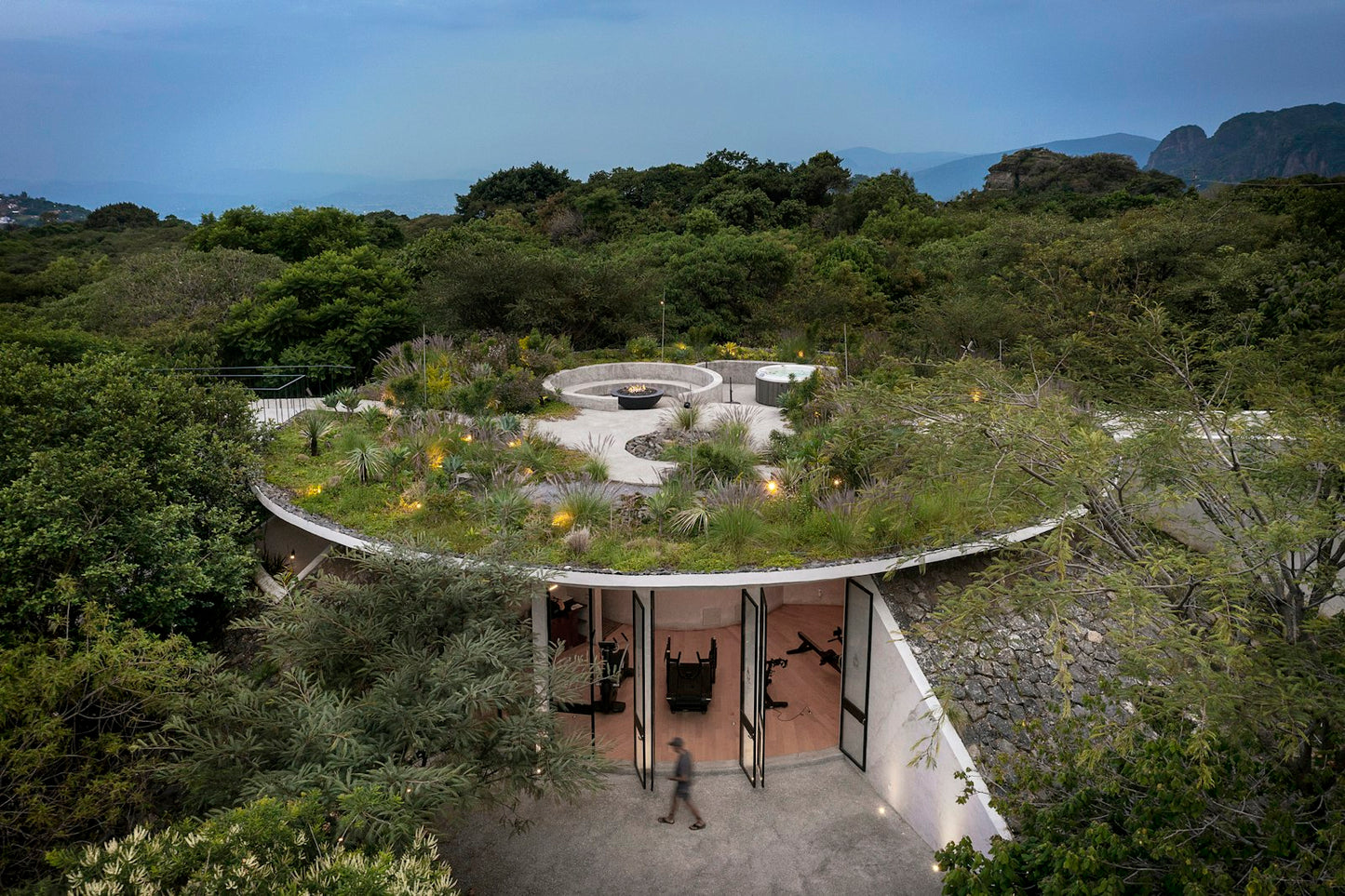 Round building with a green roof surrounded by trees and mountains