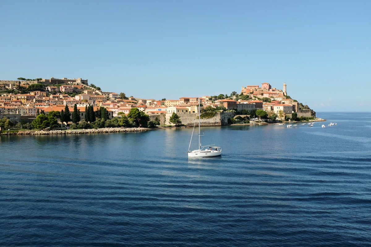 Sailing boat on calm blue water with a coastal town in the background