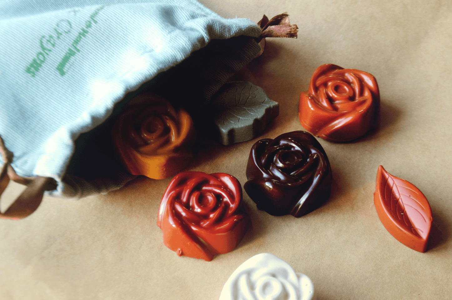 Rose-shaped soap bars in various colors on a beige surface with a branded bag.
