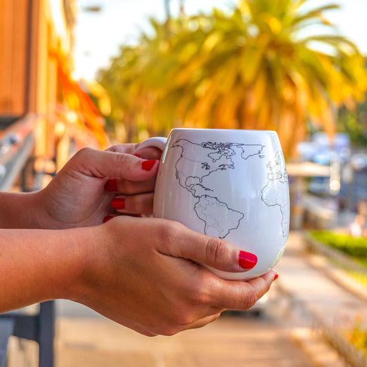 Person holding a mug with a world map design outdoors.