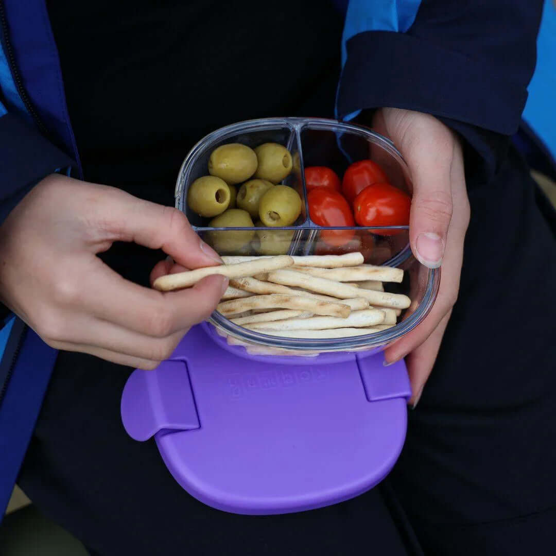 Yumbox Leakproof Snack Bowl - 3 Compartment filled with olives, tomatoes, and snacks in hand.