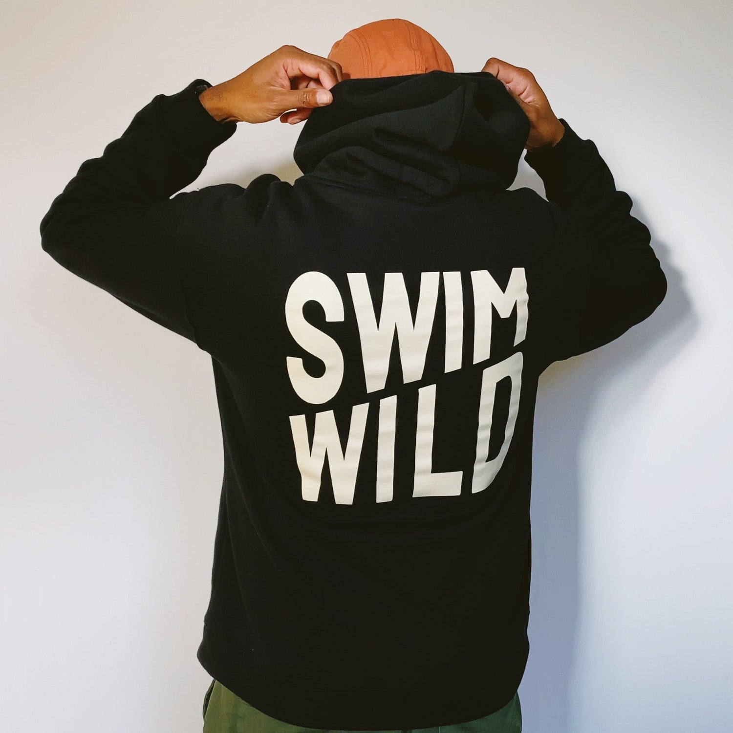 Person wearing a black hoodie with 'SWIM WILD' printed on the back, showcasing a casual lifestyle.