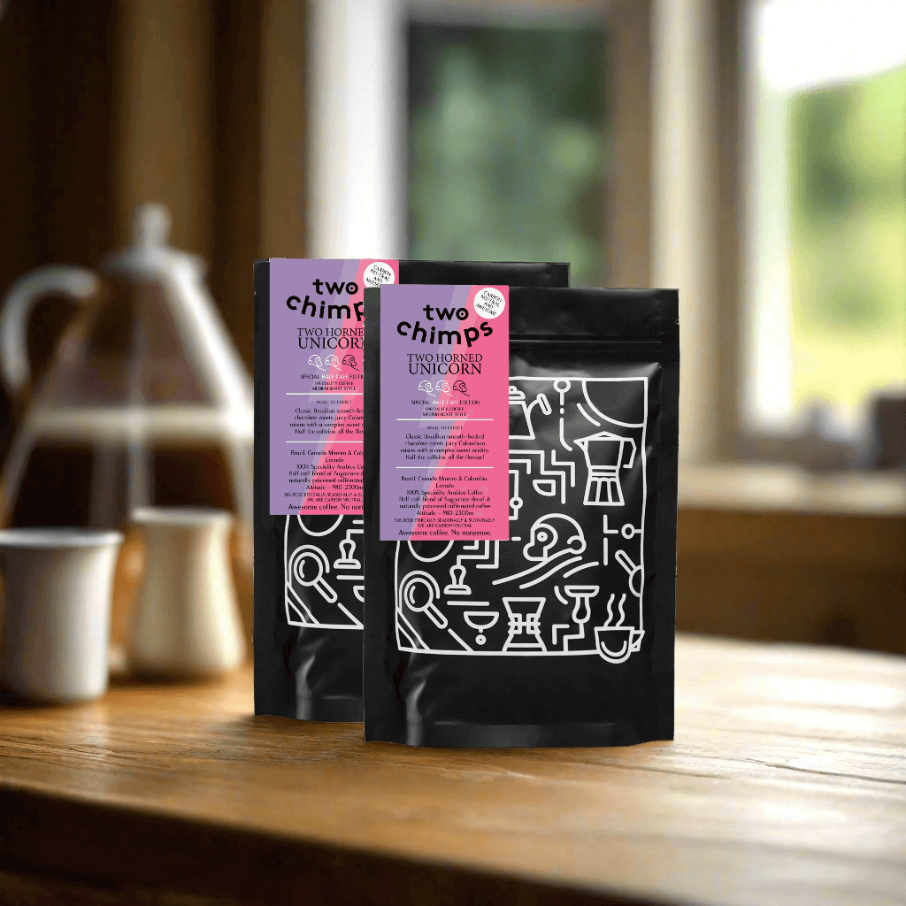 Two Chimps Coffee bags displayed on a wooden table with coffee cups in the background.