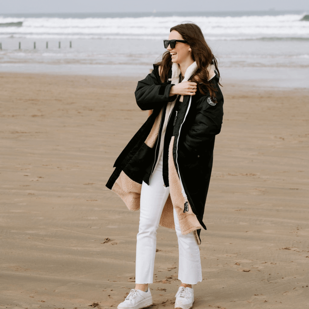 Woman in stylish outdoor jacket enjoying the beach, representing Wild & Free Outdoors sustainable gear.