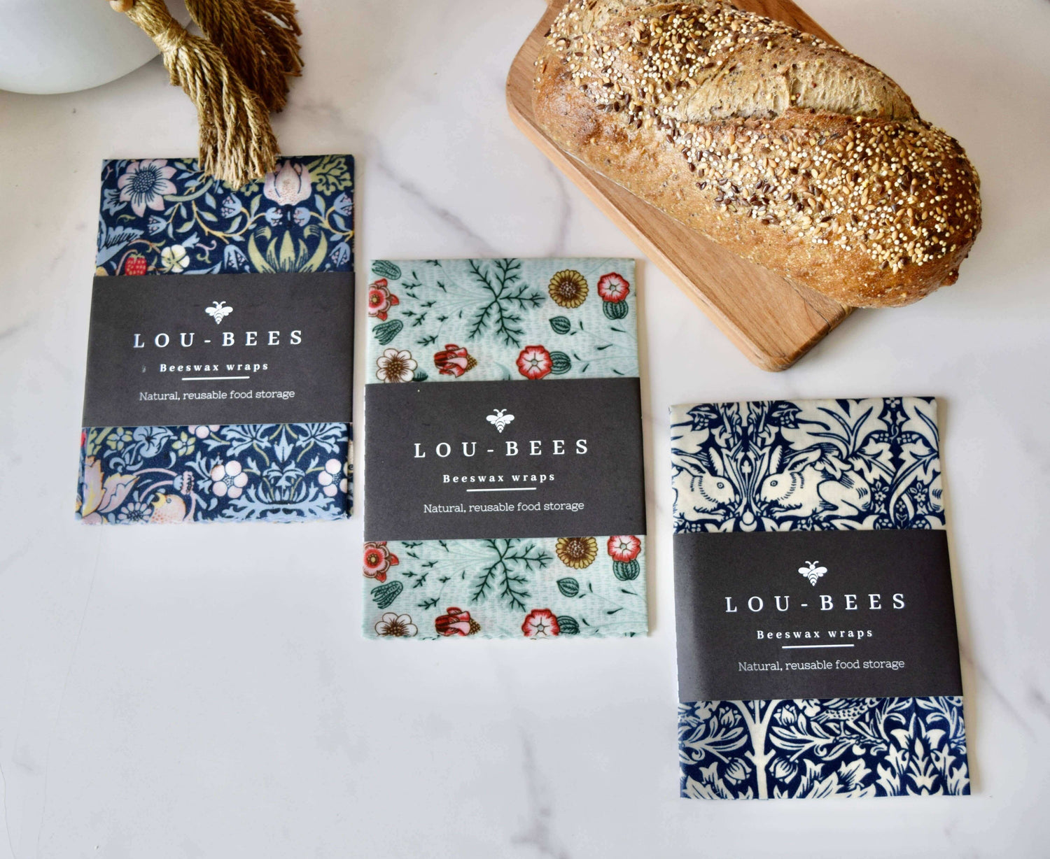 Lou-bees beeswax wraps for sustainable food storage displayed with a loaf of bread on a marble surface.