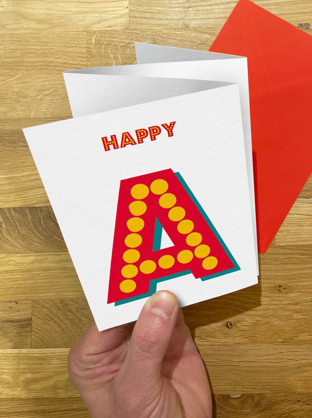 Greeting card with 'Happy A' design held by a hand on a wooden surface