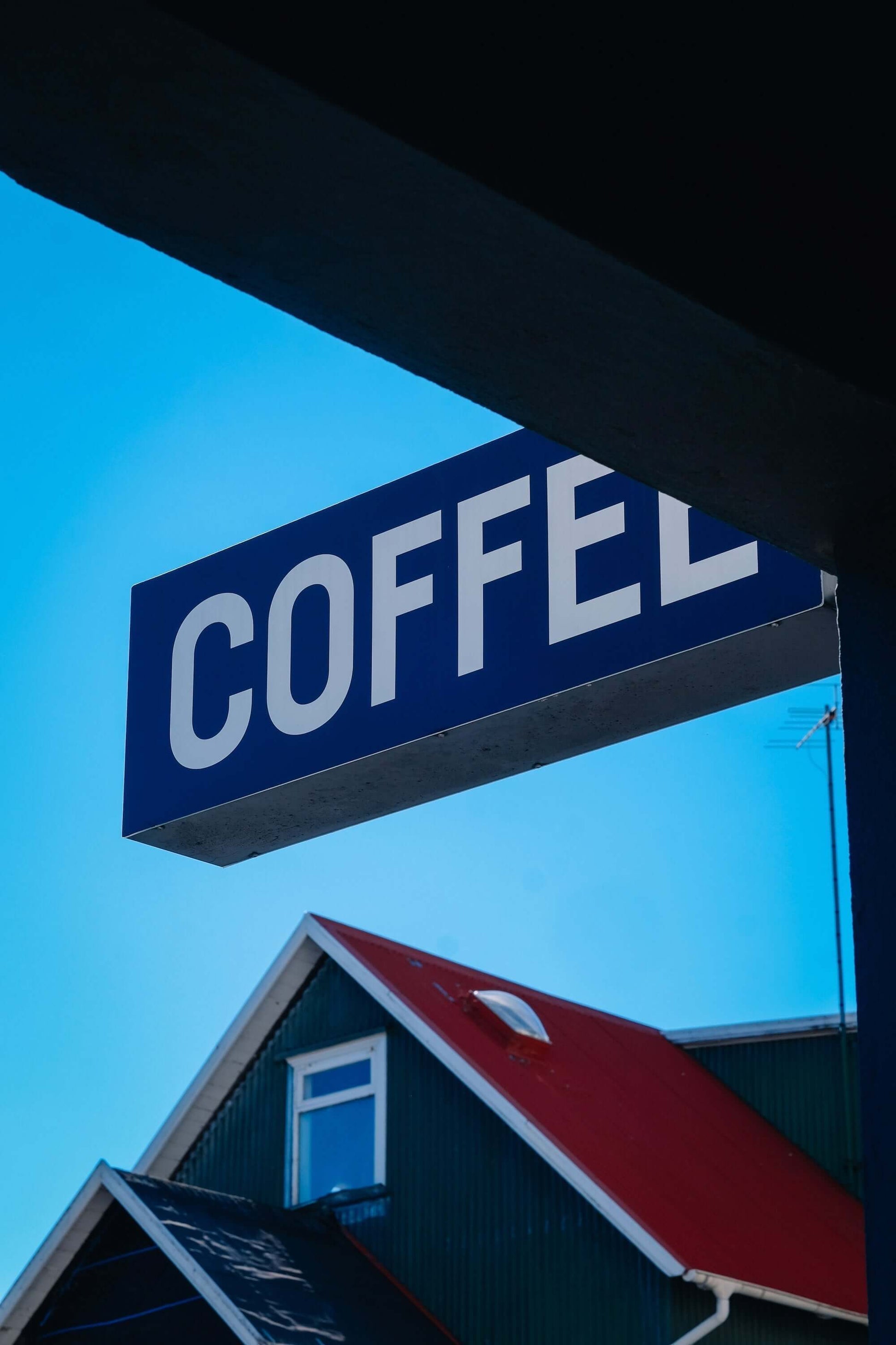 Neon coffee sign against a clear blue sky with a building in the background.