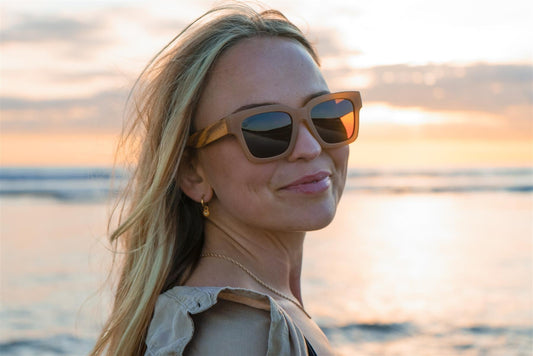 Woman wearing sunglasses with a sunset or sunrise over water in the background
