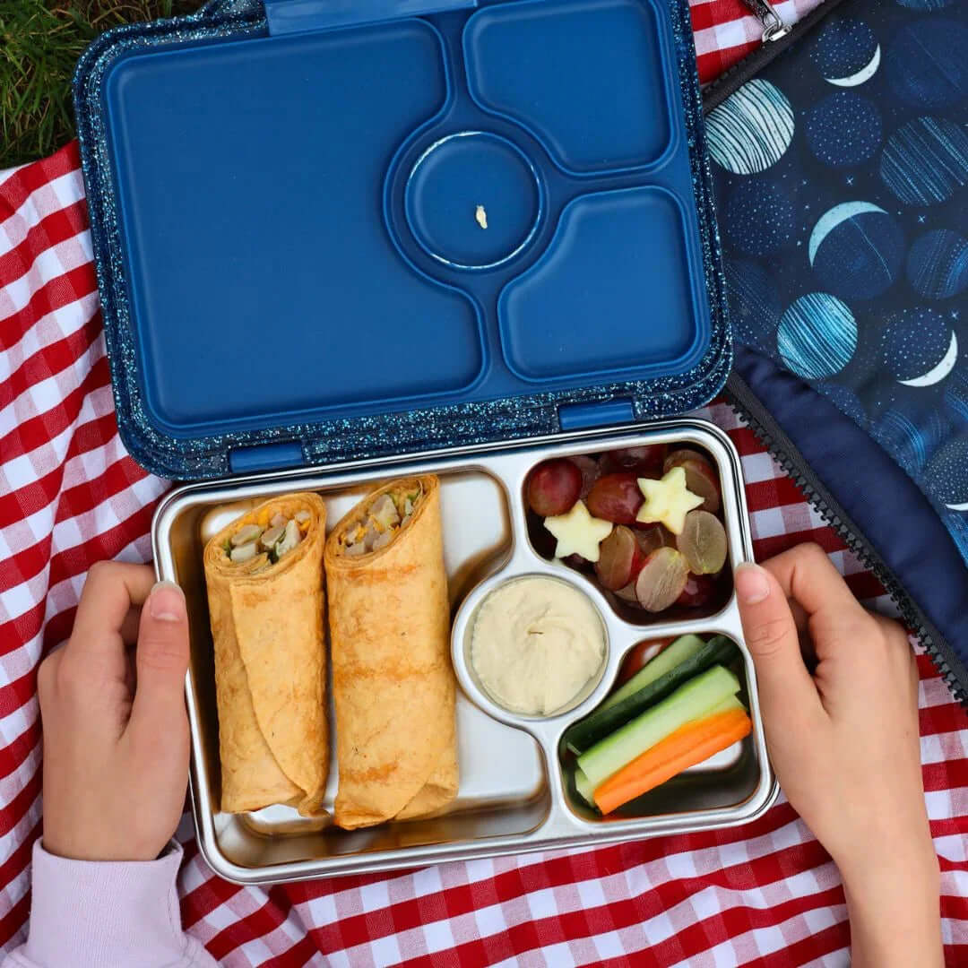 Yumbox Prêt Stainless Steel Leakproof Bento Lunch Box - Various Colours with wraps, fruits, and veggies in a picnic setting.