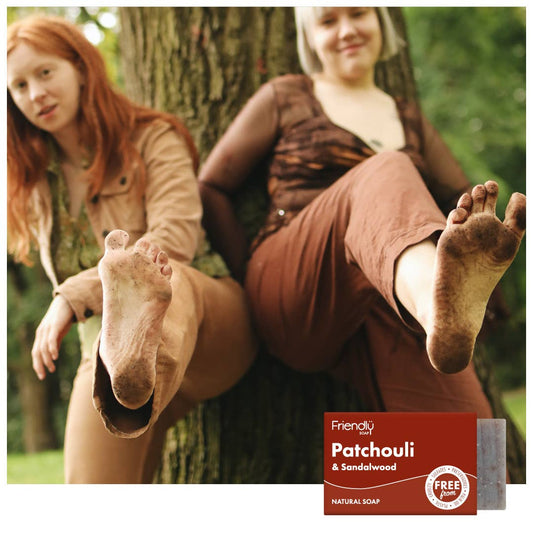 Two women sitting against a tree with a soap bar labeled 'Friendly Soap' featuring patchouli and sandalwood scents.