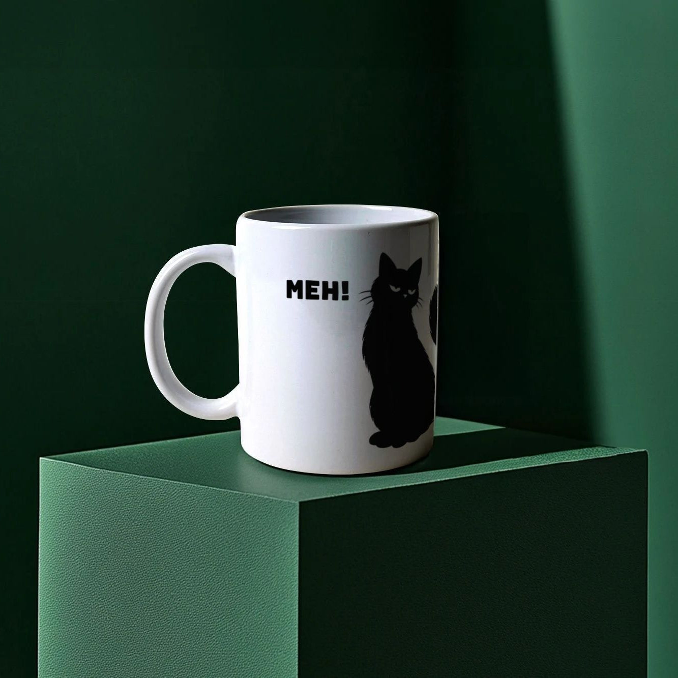 White mug with a black cat graphic and 'MEH!' text on a green surface