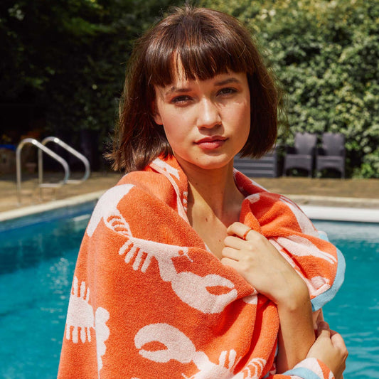 Woman wrapped in an orange towel with white lobster patterns by a pool