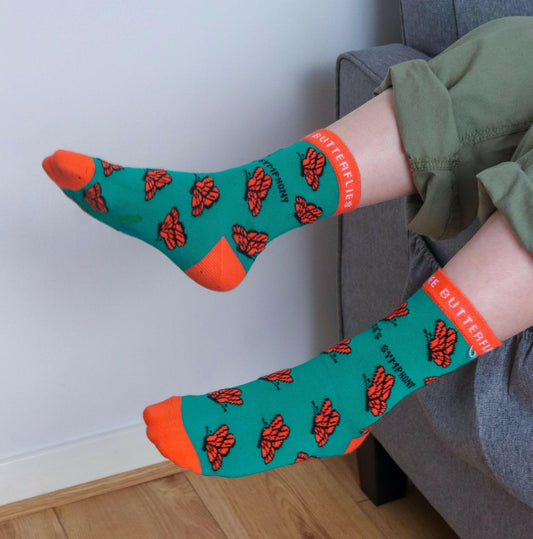 Person wearing socks with butterfly pattern and orange accents, sitting on a couch.