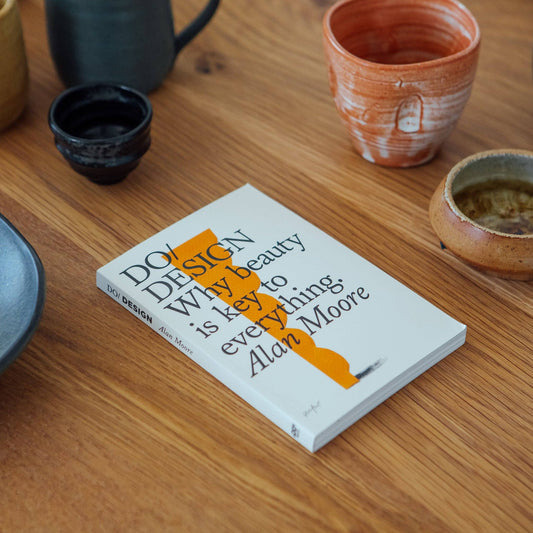 Book titled 'How Beauty is Key to Everything' by Alan Moore on a wooden table with ceramic items.
