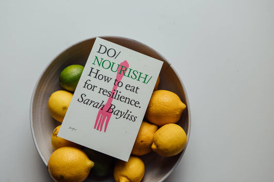 Book titled 'Do Nourish' by Sarah Bayliss surrounded by lemons and limes on a light background