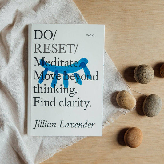 Book titled 'DO/RESET/Meditate' by Jillian Lavender on a wooden surface with stones.