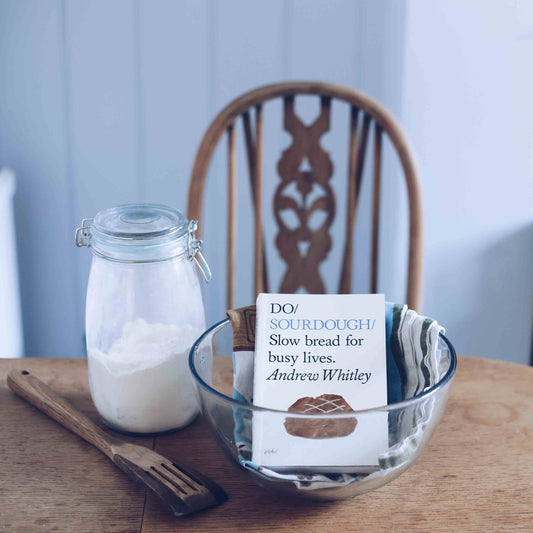 Bowl with a label, jar of flour, and wooden spoon on a table.