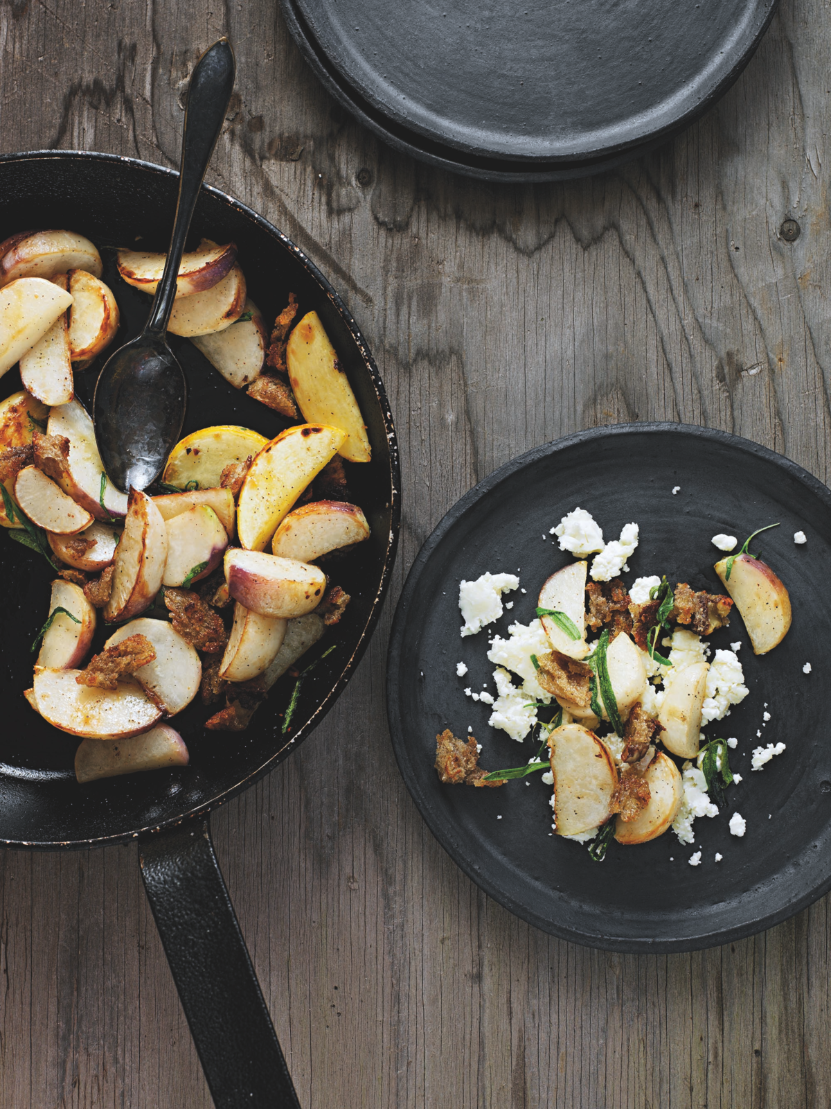 Fried apples in a skillet with a plate of food on a wooden surface