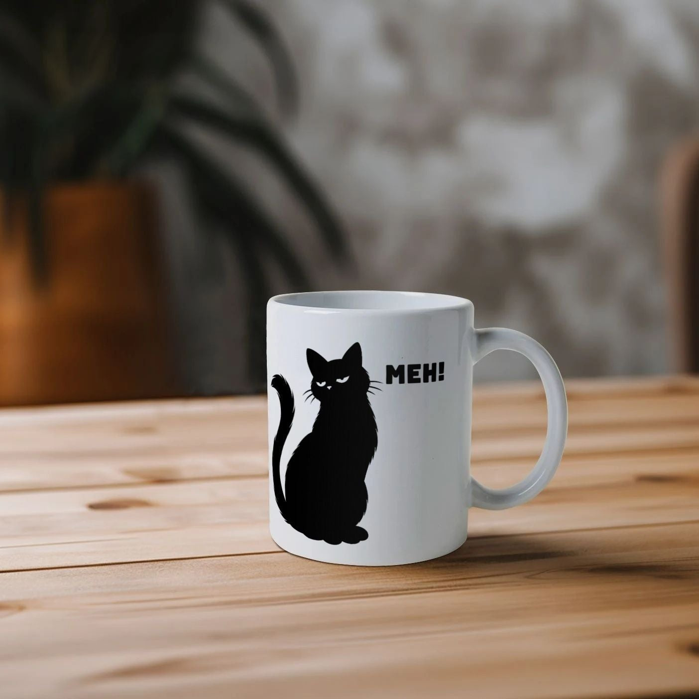 White mug with a black cat illustration and 'Meh!' text on a wooden table.