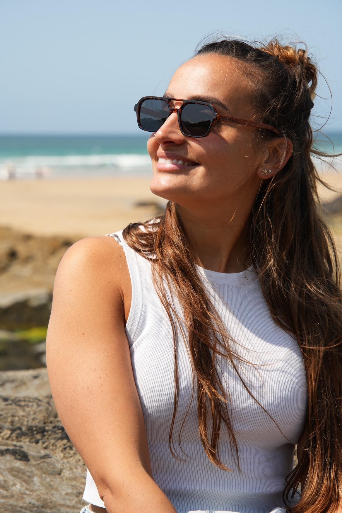 Woman wearing sunglasses and a white top on a beach