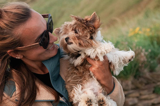 Woman holding a small dog outdoors with greenery in the background