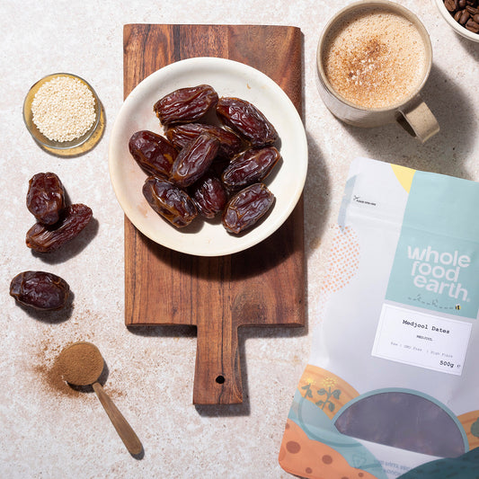 Dates on a plate with a wooden cutting board, coffee, and a Whole Foods Earth package.