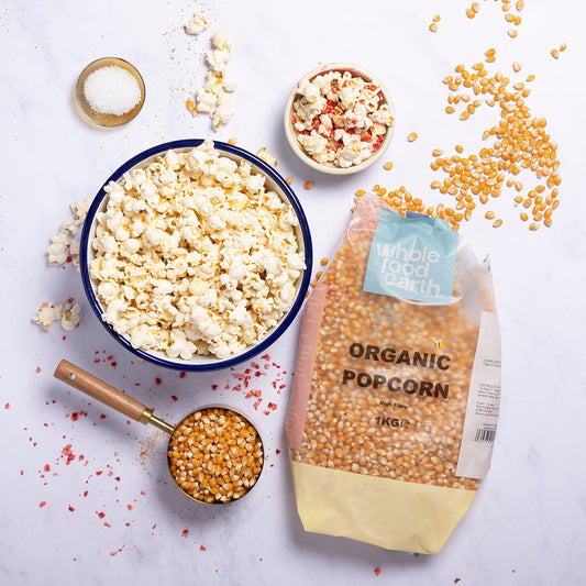 Bag of organic popcorn, bowl of popcorn, and scattered popcorn kernels on a light background