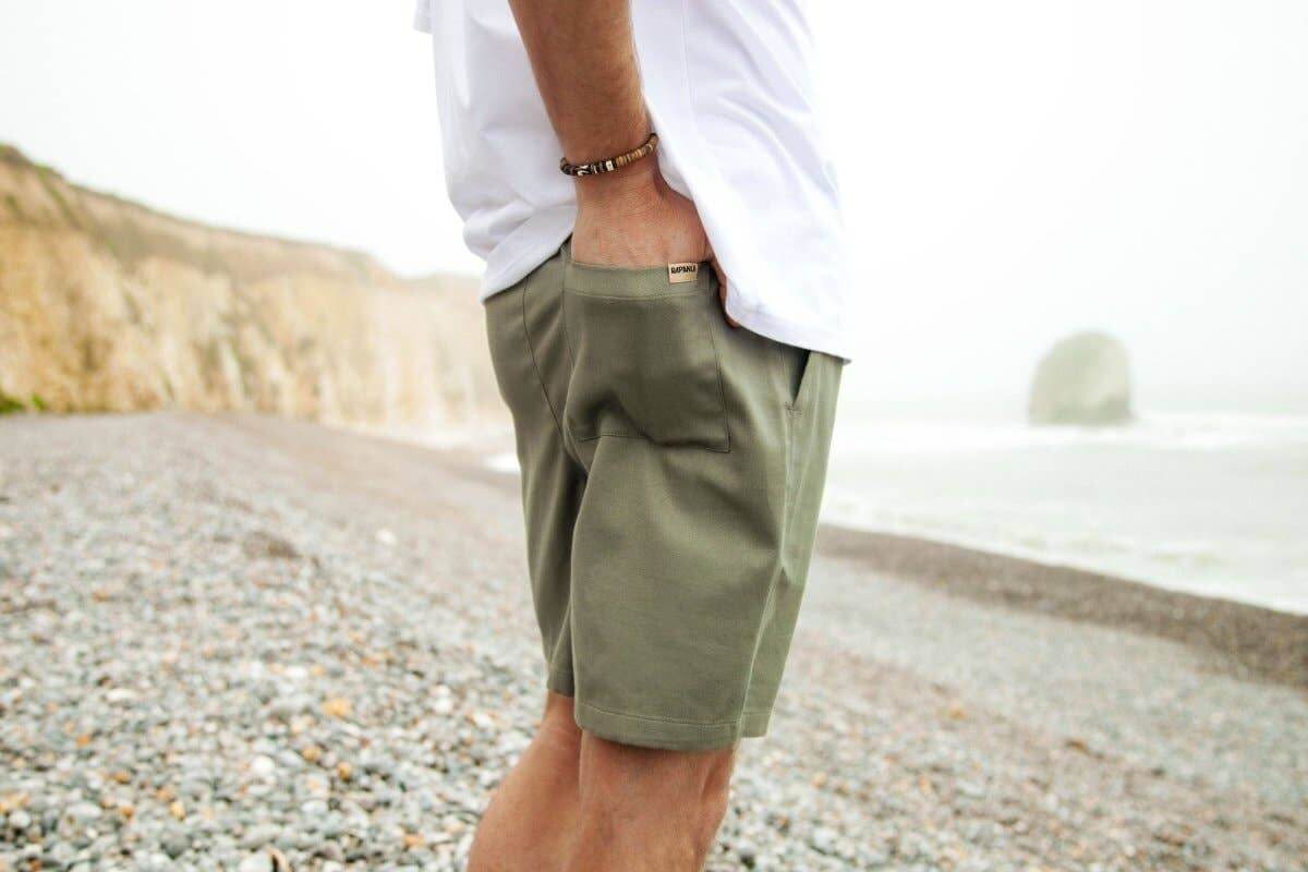 Man wearing Men's Sandbar Drawstring Organic Cotton Shorts by Rapanui on a rocky beach.