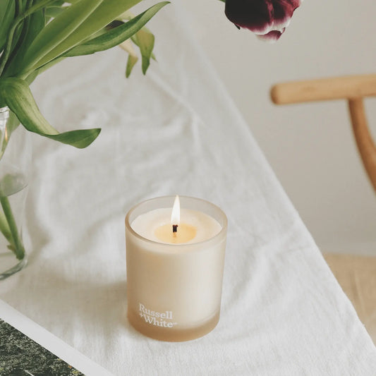 Candle in a glass holder with 'Russell & Bromley' branding on a white surface.