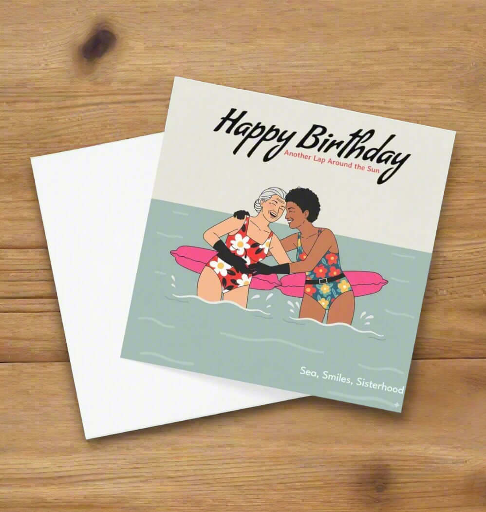 Birthday card with illustration of two people on a raft, text 'Happy Birthday, Another Lap Around the Sun', and 'Sea, Smiles, Sisterhood' on a light green background.