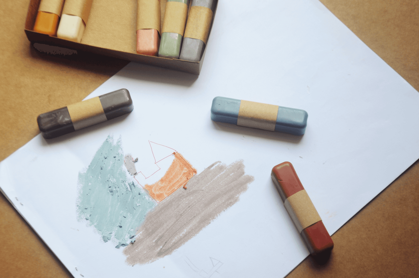 Colorful pastel crayons on a piece of paper with a wooden box in the background.