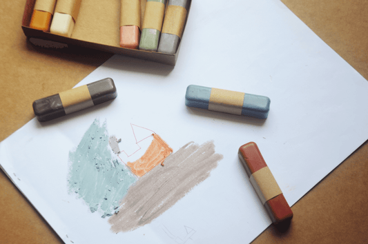 Colorful pastel crayons on a piece of paper with a wooden box in the background.