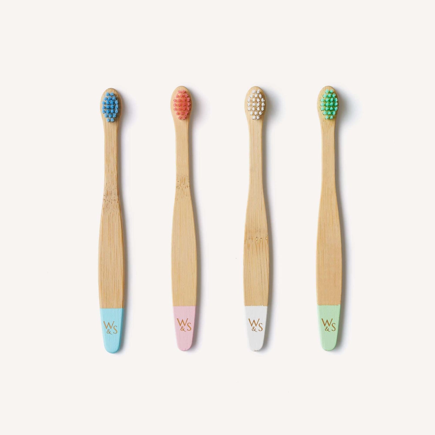 Four bamboo toothbrushes with colored bristle heads and pastel handles on a white background.