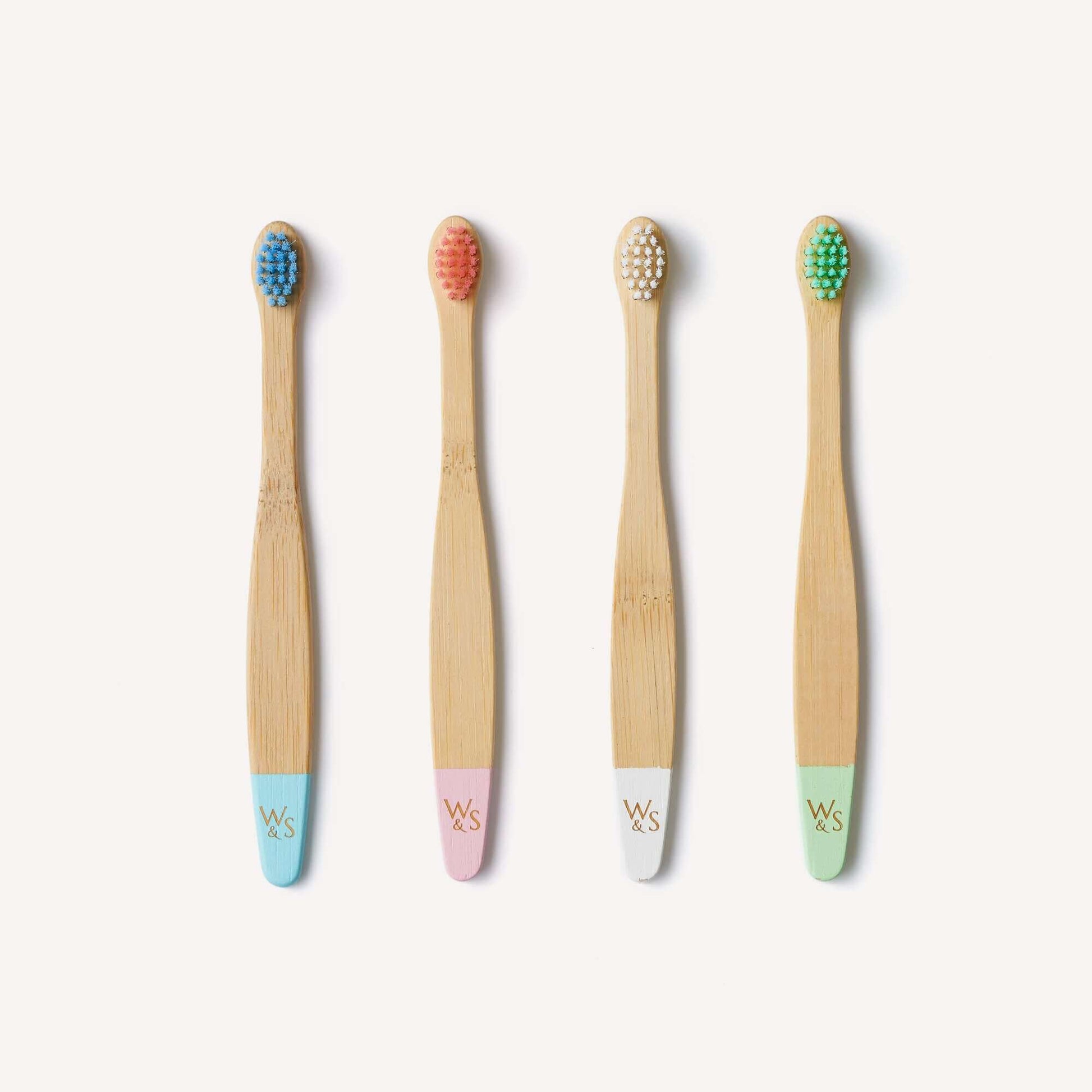Four bamboo toothbrushes with colored bristle heads and pastel handles on a white background.