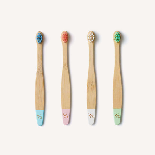 Four bamboo toothbrushes with colored bristle heads and pastel handles on a white background.