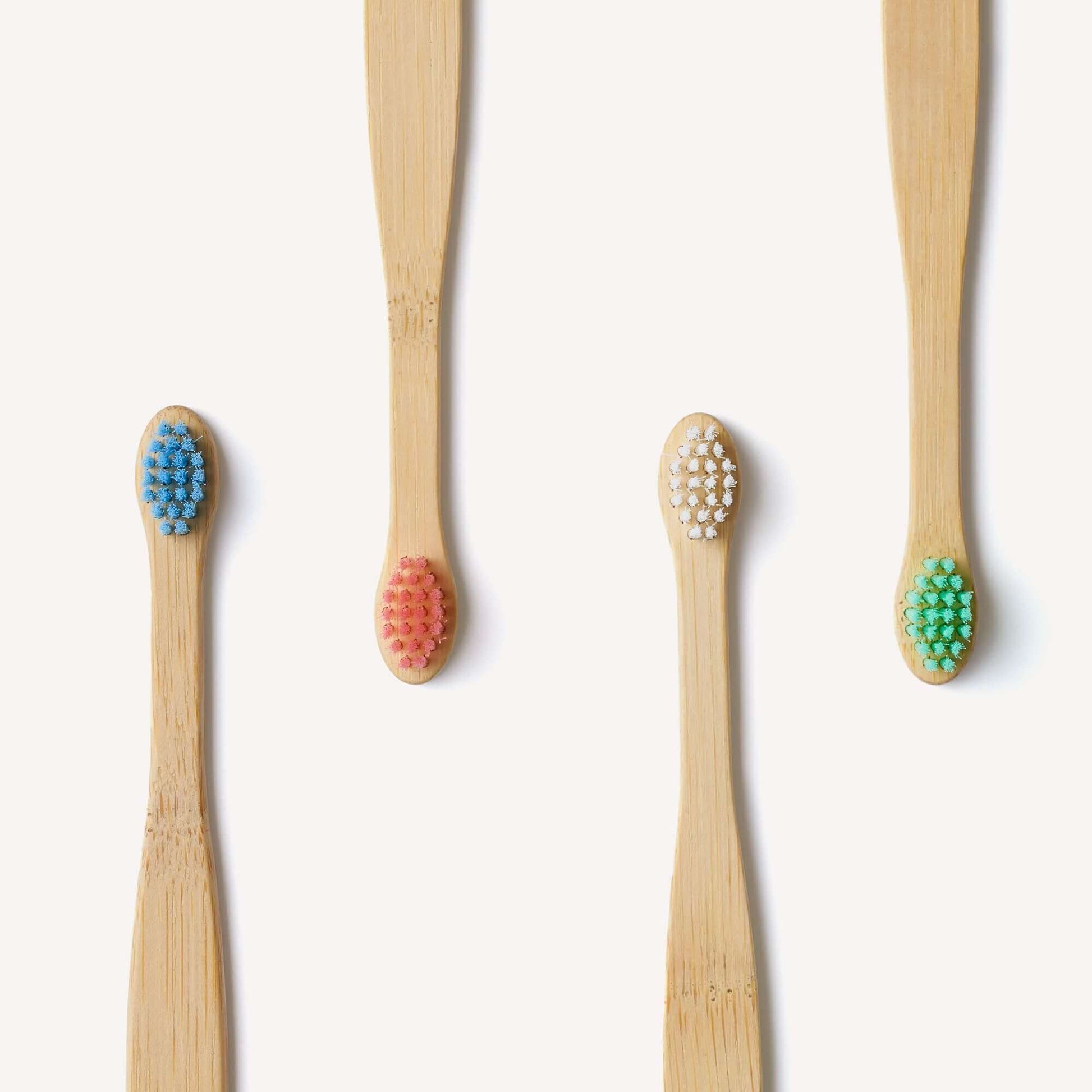 Set of four bamboo toothbrushes with colored bristle heads on a white background