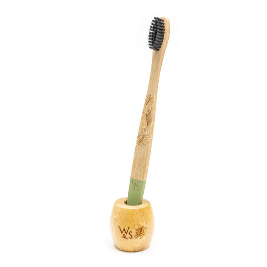 Bamboo toothbrush with black bristles in a wooden holder on a white background