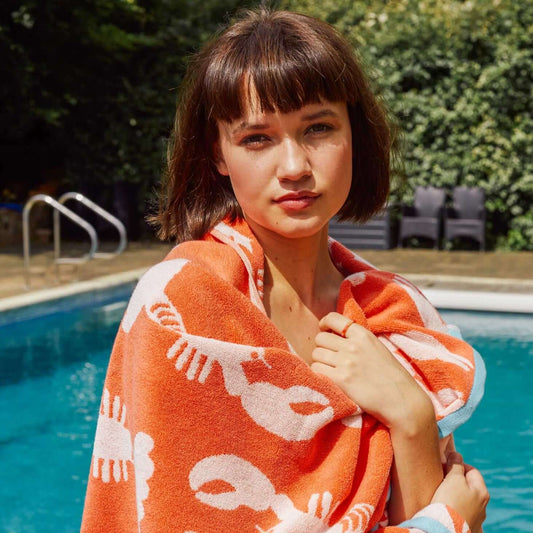 Woman wrapped in an orange towel with white lobster patterns by a pool