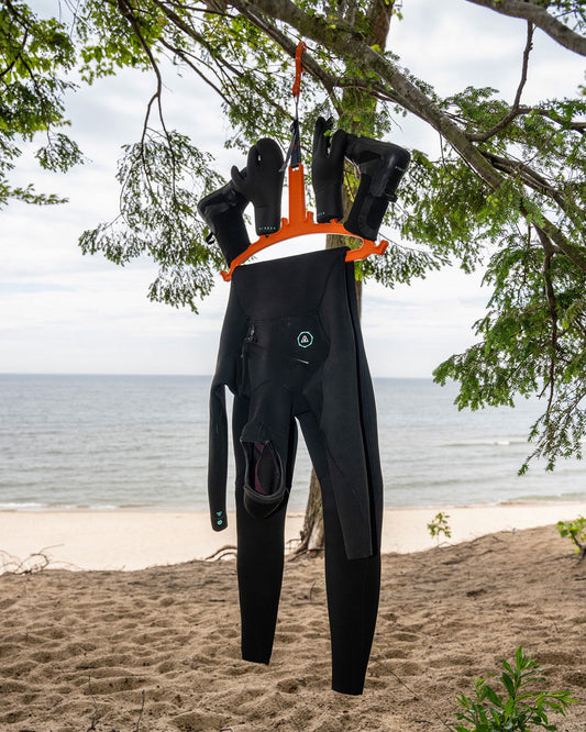 C-Monsta Wetsuit Hanger V2 - Orange (UK) holding wetsuit and boots on a beach near the water.