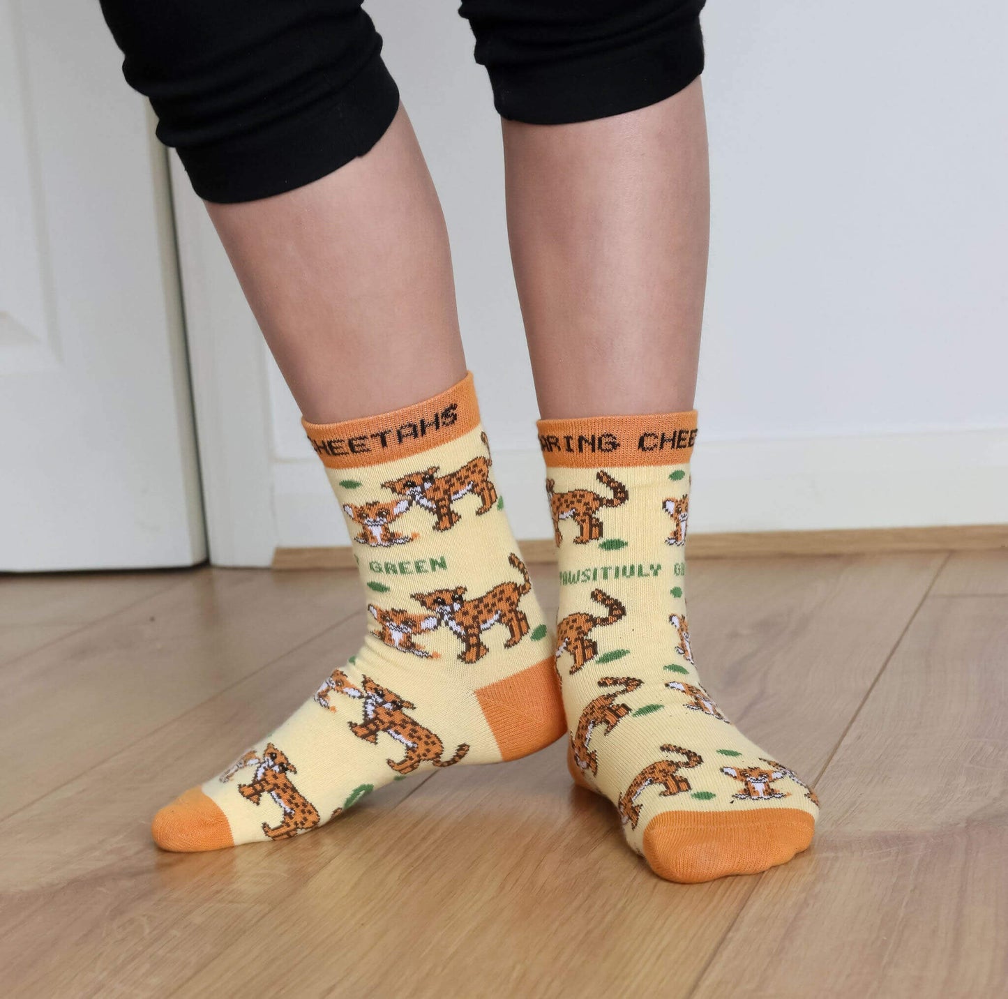 Person wearing socks with cheetah print and text on a wooden floor.