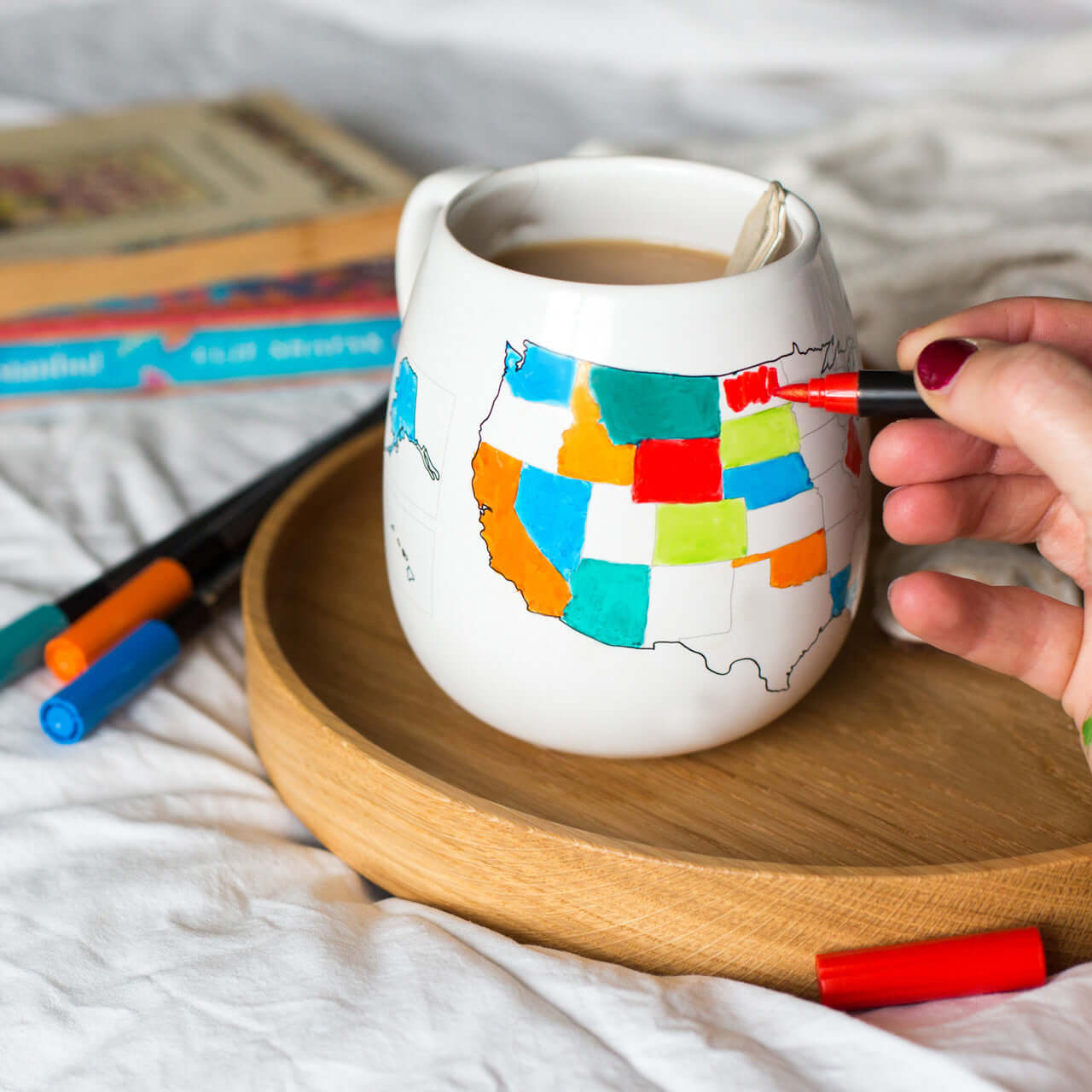 Person coloring a map of the United States on a mug with markers.